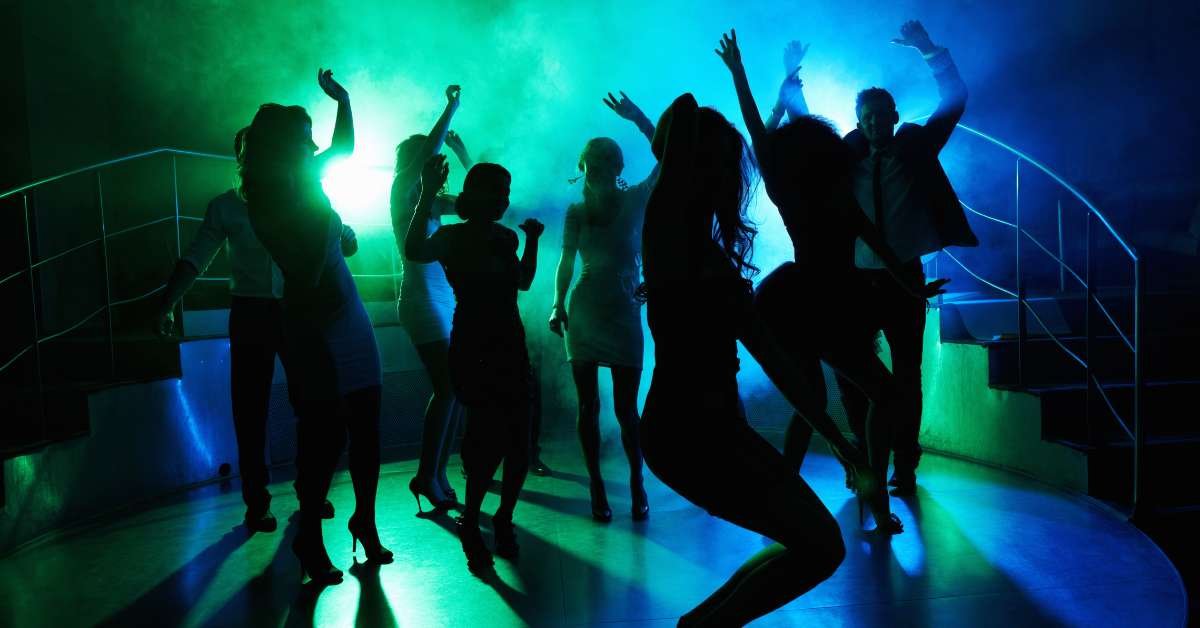 A group of people dancing energetically in a club with vibrant blue and green lighting.